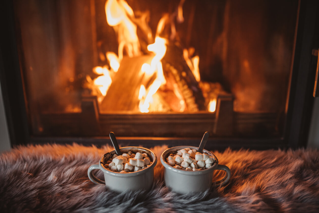 Cups with hot chocolate on fur, fireplace in background